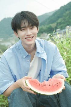 a young man sitting on the ground holding a piece of watermelon in his hand