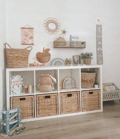 a white shelf with baskets and other items on it in a room that has wood floors