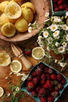 strawberries, lemons and daisies in bowls on a wooden table with flowers