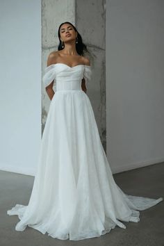 a woman in a white wedding dress standing next to a wall with her hands on her hips