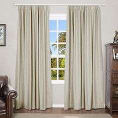 a living room with a chair and window covered in white drapes that are open to the outside