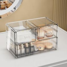 a clear container filled with donuts sitting on top of a white counter next to a mirror