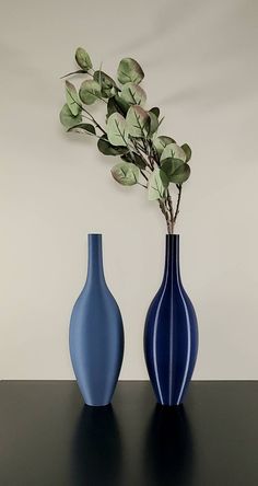 two blue vases sitting on top of a black table next to each other with green leaves in them