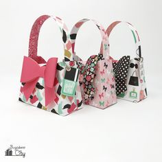 three small bags with bows are lined up on a white surface, one is pink and the other has black and white polka dots