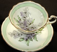 two tea cups and saucers with flowers painted on the sides, one is green