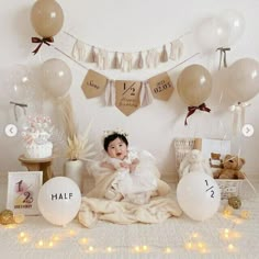 a baby is sitting on the floor surrounded by balloons and other items for her first birthday