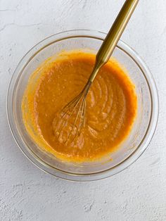 a whisk in a glass bowl filled with orange sauce on a white surface