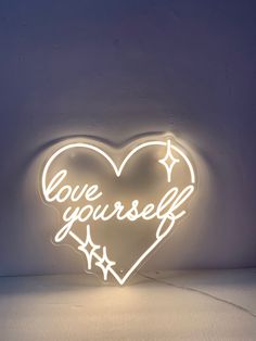 a heart shaped neon sign with the words love yourself written in white letters on it