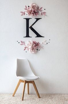 a white chair sitting in front of a wall mounted letter k with flowers on it