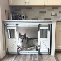 a dog is laying down in his kennel under the counter top on the kitchen floor