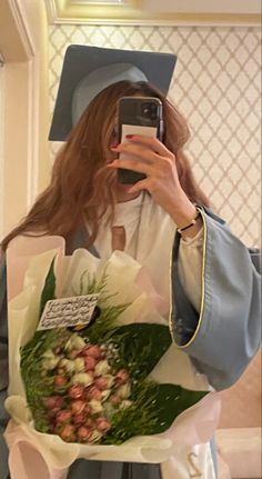 a woman taking a selfie with her graduation cap and gown holding a bouquet of flowers