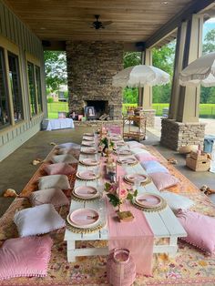 a long table set up with pink and white place settings for an outdoor dinner party