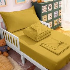 a bed with yellow sheets and pillows in a room next to a teddy bear on the floor