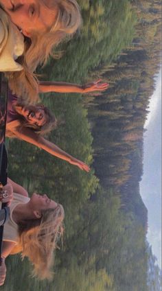 two women standing next to each other in front of a body of water with trees