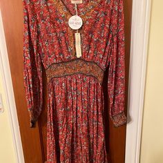 A Showstopping Bohemian Maxi Dress In A Mixed Floral Print, Featuring Voluminous Long Sleeves With A Smocked Elastic Cuff, A Flattering V-Neckline, And A Smocked Elastic Waist For Definition. The Contrast Floral Print Paneled Skirt Adds Shape And Movement To This Showstopping Style. Stock Photos Show The Style And Cut, And The Last Three Pictures Show The Actual Color, A Lovely Burnt Red Floral Design. Bohemian Paisley Print Midi Dress For Fall, Bohemian Long Sleeve Midi Dress With Paisley Print, Bohemian Knee-length Paisley Print Dress, Red Bohemian Maxi Dress With Paisley Print, Bohemian Midi Boho Dress In Rayon, Bohemian Midi-length Rayon Boho Dress, Bohemian Style Midi Boho Dress In Rayon, Fitted Bohemian Rayon Midi Dress, Boho Print Midi Dress In Rayon