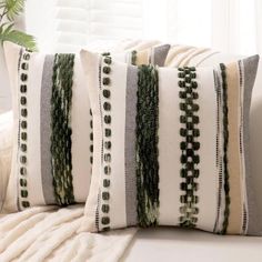 two pillows sitting on top of a white couch next to a potted plant in front of a window