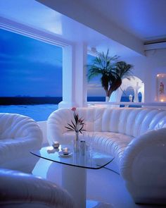 a living room filled with white furniture next to the ocean