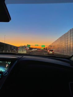 the sun is setting over an interstate with cars driving on it and traffic signs in the distance