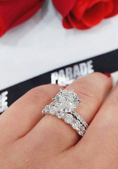 a close up of a person's hand with a ring on it and a rose in the background