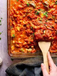 a wooden spoon in a casserole dish with meat and tomato sauce on it