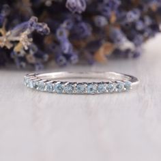 a white gold wedding band with blue topazte stones on the side and lavender flowers in the background