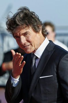 a man in a suit and tie making a hand gesture with his right hand while standing on the red carpet