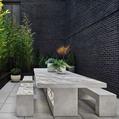 an outdoor table and benches in front of a black brick wall with plants on it