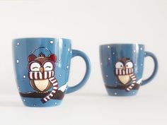 two coffee mugs decorated with owls and snowflakes on blue cups, one has a striped scarf around its neck