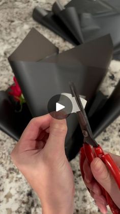 someone is cutting paper with scissors on a table next to some black vases and flowers