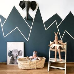 a baby sitting in a basket next to an elephant head and mountains on the wall