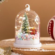 a small christmas tree in a snow globe on a table with other ornaments and decorations