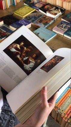 a person is holding an open book in front of many books on the table with them