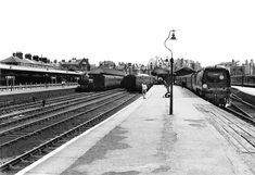 black and white photograph of two trains at a train station with people walking on the platform