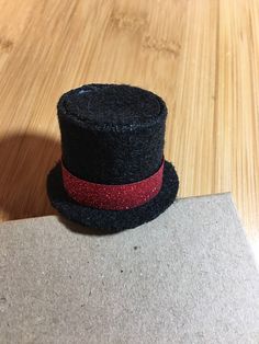 a small black hat with a red ribbon around the brim on a wooden surface