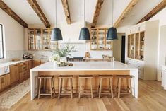 a large kitchen with wooden floors and white counter tops, two pendant lights over the island