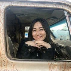 a woman sitting in the passenger seat of an old truck with rusted paint on it