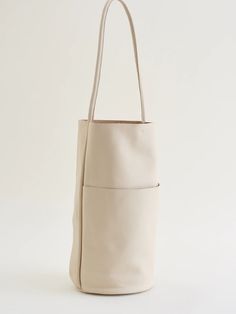 A best seller from Are Studio's Core Collection that has been with them since the beginning. A bucket style shoulder bag with a circular base and minimal look. One rolled handle is integrated into the side seams of the bag with one large exterior pocket. Unlined cowhide leather with raw edges. SIZE 16" tall × 12.5" wide (at top) × 8" deep Strap drop is 13" COMPOSITION 100% Leather CARE Leather Care Are Studio offers two types of leather: a vegetable tanned semi-aniline leather for soft form bags and an oil finish semi-vegetable leather in matte for structured bags. Each of the hides has unique characteristics and can include variations in color, texture and markings. These sometimes remain visible due to our minimal intervention approach to treating leather in an effort to avoid using hars Minimalist Leather Bucket Bag With Double Handle, Travel Bucket Bag With Rolled Handles, Travel Bucket Bag In Beige With Smooth Grain, Chic Bucket Hobo Bag With Rolled Handles, Minimalist Bucket Bag For Work, Minimalist Bucket Tote Bag For Work, Minimalist Tote Bucket Bag For Work, Minimalist Cream Tote Shoulder Bag, Beige Smooth Grain Bucket Bag Tote