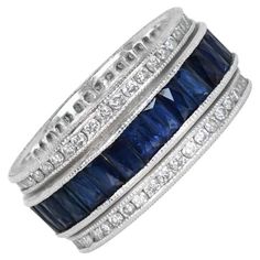 An enchanting eternity band showcasing channel-set elongated French-cut natural sapphires. Rows of channel-set round brilliant diamonds elegantly border the sapphires, creating a captivating design with stones set both above and below. Crafted in platinum, the band is adorned with intricate hand engravings and fine milgrain detail, adding a touch of timeless elegance. Ring Size: 6.5 US, Resizable Metal: Platinum Stone: Diamond, Sapphire Stone Cut: French Cut, Round Brilliant Cut Style: Art Deco Total Weight: 10.3 Grams Width Of Band: 8.77mm Band Style: Eternity Band Diamond Eternity Band, French Cut, Eternity Band Ring, Channel Set, Eternity Band Diamond, Sapphire Stone, Diamond Eternity, Stone Cuts, Eternity Band