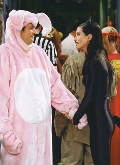 two people dressed in costumes standing next to each other on the street, one wearing a pink bunny costume