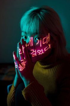 a woman is holding her face up with neon writing on the side of her face