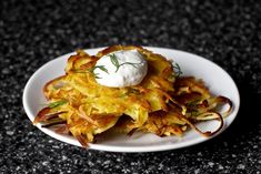 a white plate topped with potato fritters covered in sour cream and garnished with herbs