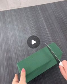 someone cutting paper with a pair of scissors on top of the green object in front of them