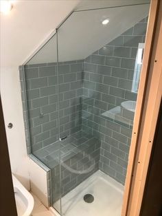 a glass shower door in a bathroom next to a white sink and toilet with grey tiles on the walls