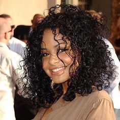 a close up of a person wearing a brown shirt and smiling at the camera with other people in the background