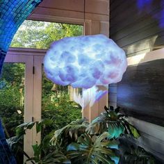 a cloud shaped light hanging from the side of a building next to a planter filled with potted plants