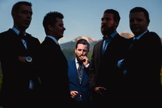 a group of men standing next to each other wearing suits and ties in front of mountains