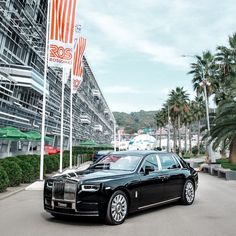 a black rolls royce parked in front of a tall building with american flags on it