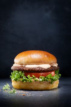 a hamburger with lettuce, tomato and mayonnaise sitting on a black surface