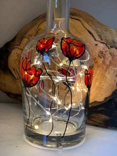 a glass vase with red flowers and fairy lights in it on top of a table