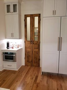 a kitchen with wooden floors and white cupboards next to a door that leads to another room